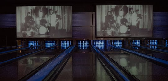 Bowling lanes with pins and music videos above