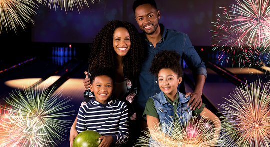 Family holding bowling balls and smiling on the lanes overlayed with fireworks