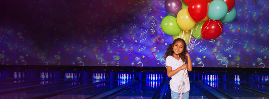 little girl holing balloons in front of a bowling alley