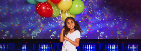 little girl holding balloons in front of a bowling alley