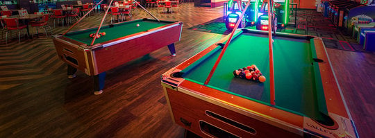 Billiards table with balls racked and cues above