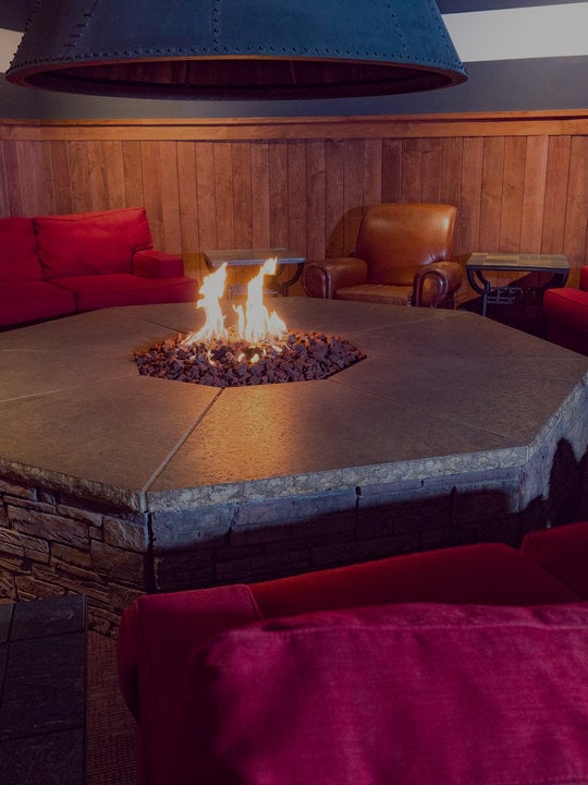 Comfy maroon couches around a fire pit with flames