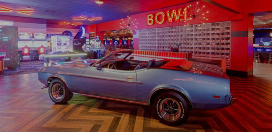 Blue vintage car inside a bowling alley with an arcade in the background