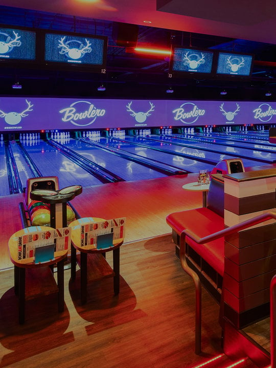 view down bowling lanes from a seating area with stools