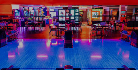 view of bowling ball racks, tables, and a neon lit arcade area