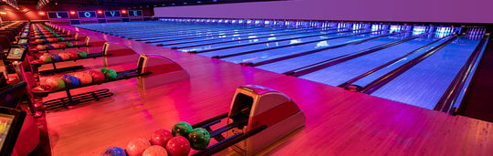 rows of neon light bowling lanes and bowling balls in racks