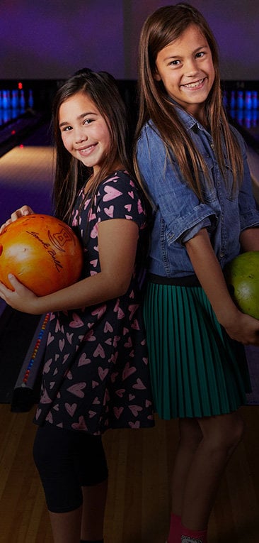 Two young girls smiling and holding bowling balls