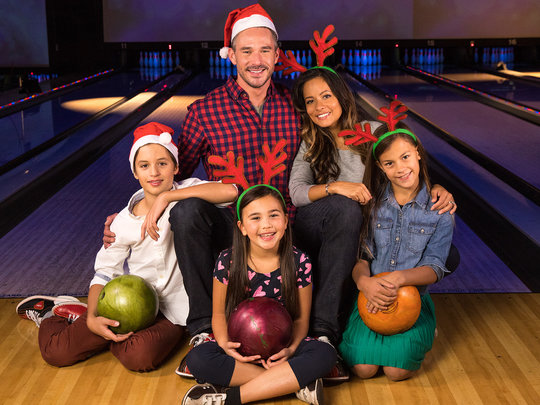 Family posing on the lanes with bowling balls and Christmas attire