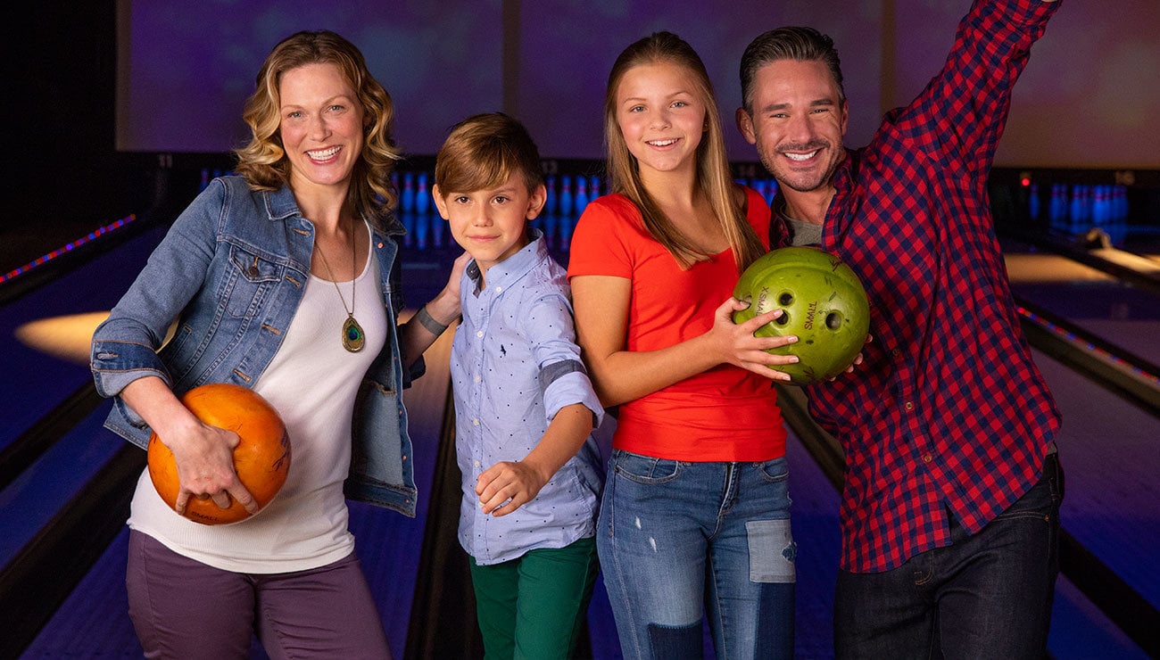 Mom and dad smiling with son and daughter holding bowling balls